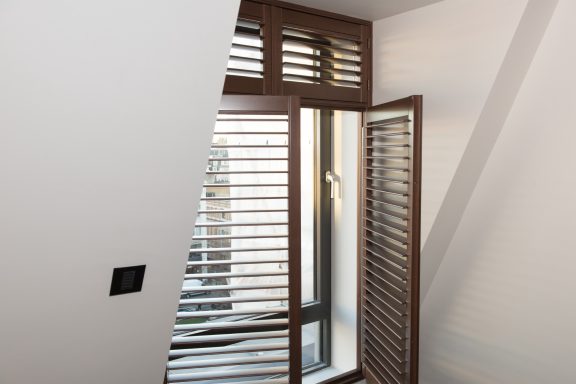 Hardwood in dark shade. Window with wooden shutters and a slanted wall, allowing natural light indoors.