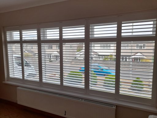 No limits on size. These are 63mm lourves hardwood. Modern window with slatted blinds, showing a street view outside with vehicles and greenery.